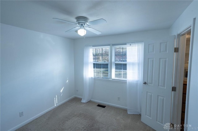 carpeted empty room with baseboards, visible vents, and a ceiling fan