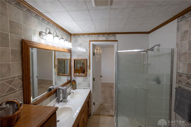 bathroom with tile walls, visible vents, ornamental molding, a sink, and a shower stall