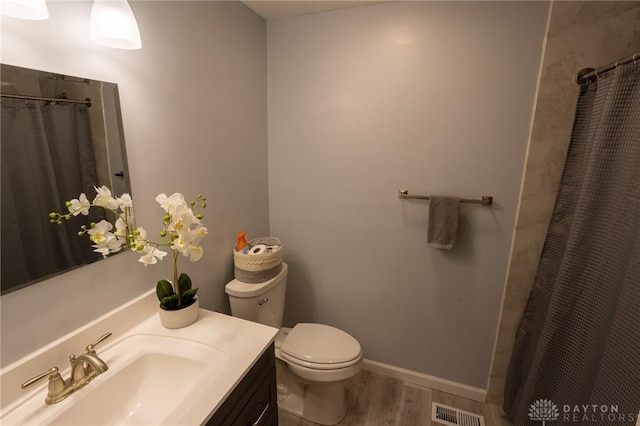 bathroom featuring visible vents, toilet, vanity, wood finished floors, and baseboards