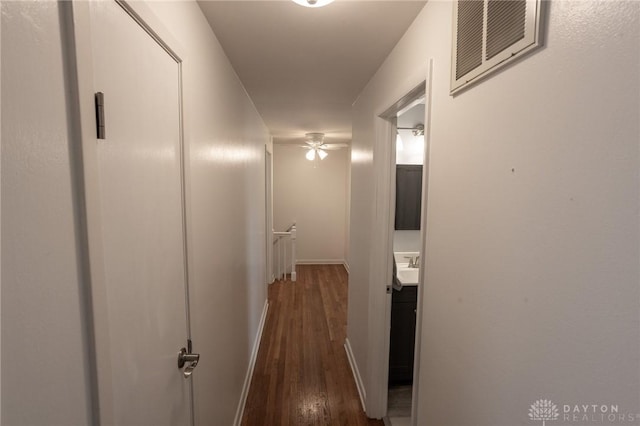 hallway with visible vents, dark wood-type flooring, a sink, an upstairs landing, and baseboards