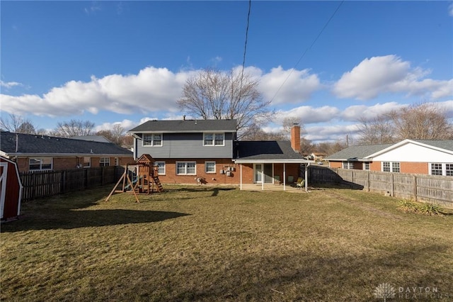 back of property featuring a yard, a fenced backyard, a playground, and brick siding