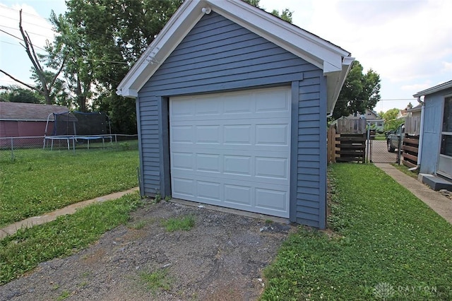 detached garage featuring driveway, a trampoline, and fence