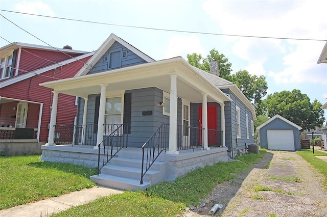 bungalow featuring an outbuilding, covered porch, a detached garage, driveway, and a chimney