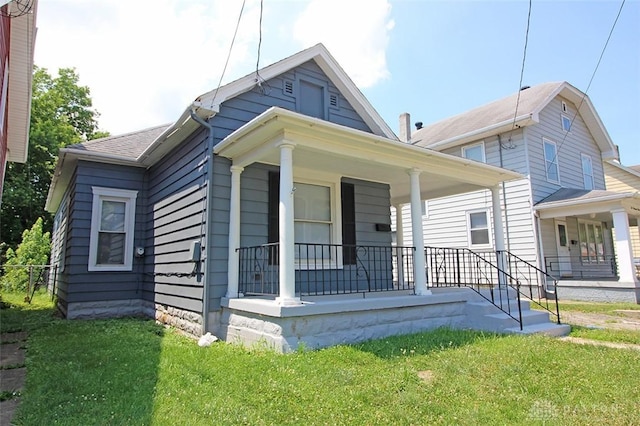 view of front facade with covered porch, a shingled roof, and a front yard