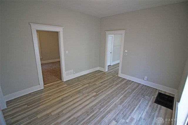 spare room featuring wood finished floors, visible vents, and baseboards