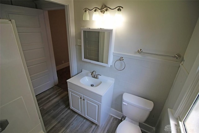 bathroom featuring tile walls, toilet, wainscoting, vanity, and wood finished floors