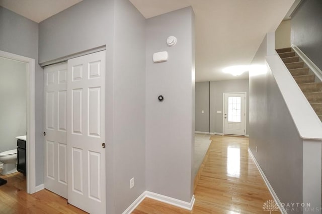 hall with light wood-type flooring, baseboards, and stairway