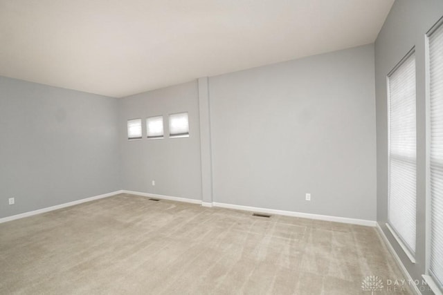 empty room featuring baseboards, visible vents, and light colored carpet