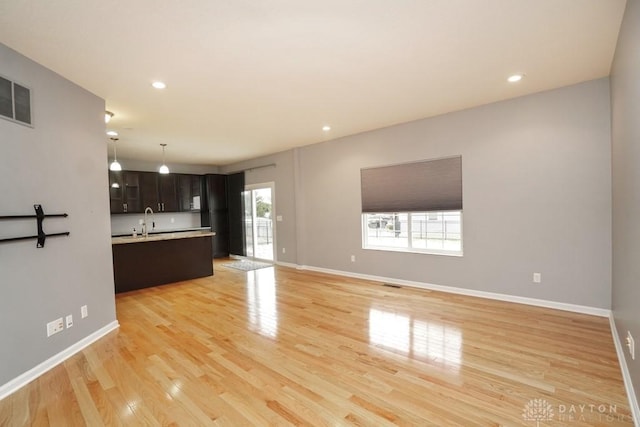 unfurnished living room featuring light wood-type flooring, baseboards, a sink, and recessed lighting