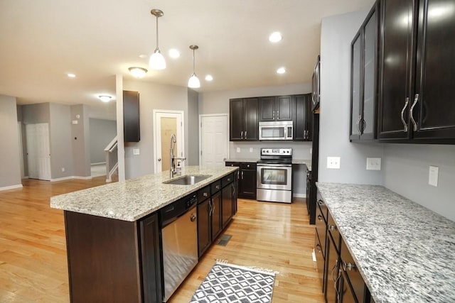 kitchen featuring decorative light fixtures, stainless steel appliances, light wood-style flooring, a sink, and an island with sink