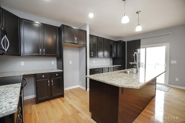 kitchen with light stone counters, a sink, baseboards, light wood finished floors, and decorative light fixtures