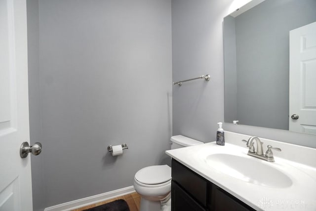 half bathroom with wood finished floors, vanity, toilet, and baseboards