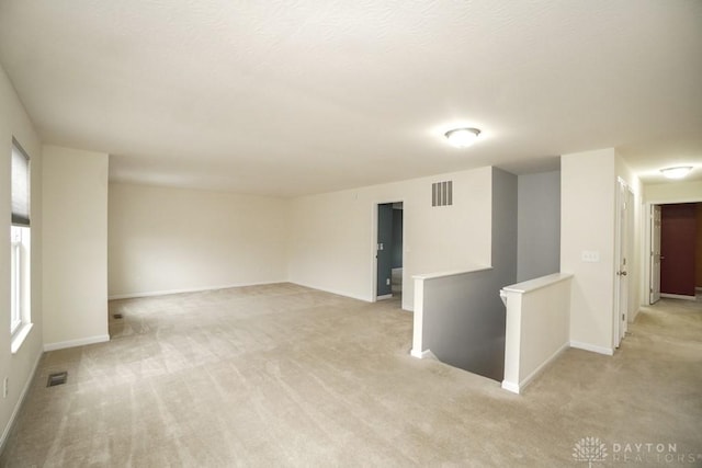 spare room featuring light carpet, visible vents, and baseboards