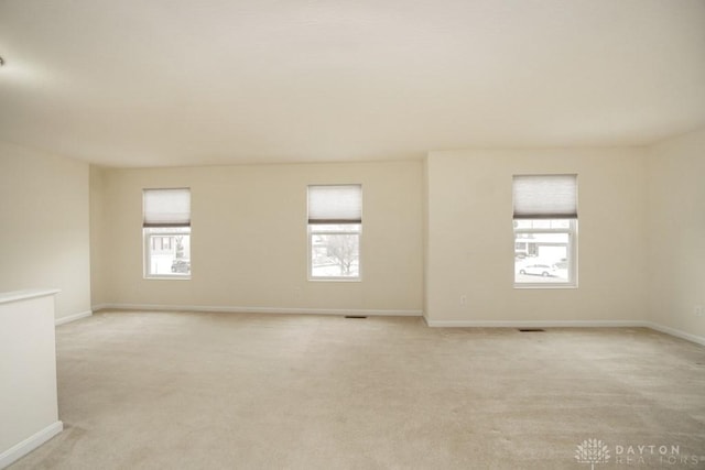 empty room with baseboards, visible vents, and light colored carpet