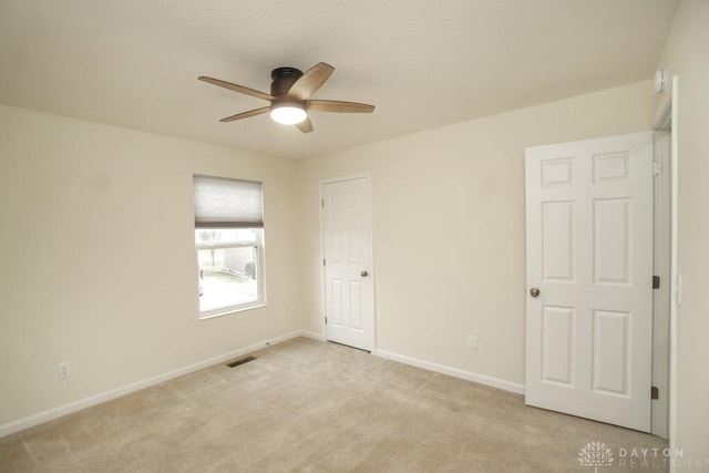 spare room with light colored carpet, ceiling fan, visible vents, and baseboards