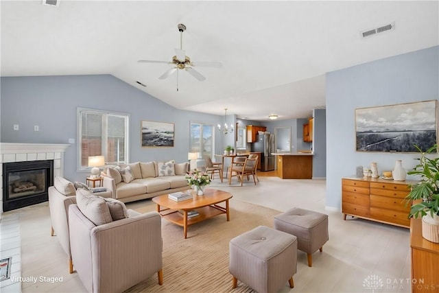 living area with ceiling fan with notable chandelier, lofted ceiling, visible vents, and a tile fireplace