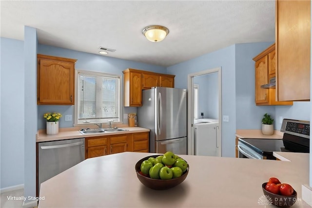 kitchen featuring appliances with stainless steel finishes, washing machine and clothes dryer, light countertops, a sink, and exhaust hood