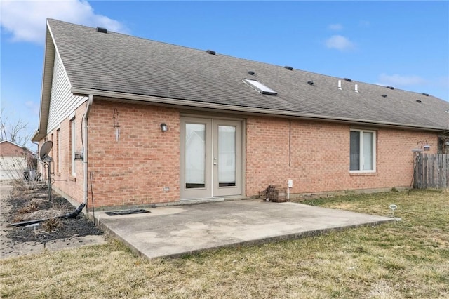 rear view of house with a shingled roof, a patio area, fence, and brick siding