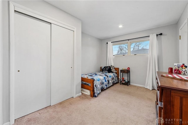 bedroom with baseboards, a closet, and light colored carpet