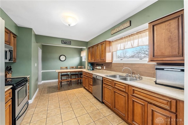 kitchen with light tile patterned flooring, a sink, light countertops, appliances with stainless steel finishes, and brown cabinets