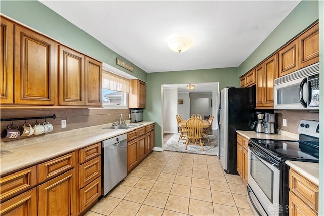 kitchen featuring light tile patterned floors, light countertops, appliances with stainless steel finishes, brown cabinetry, and a sink