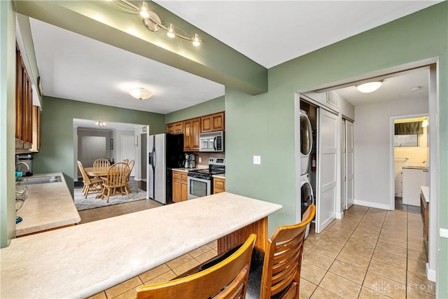 kitchen featuring stacked washer and dryer, light tile patterned floors, appliances with stainless steel finishes, light countertops, and a sink