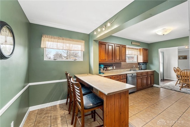 kitchen with brown cabinets, a kitchen breakfast bar, a peninsula, light countertops, and stainless steel dishwasher