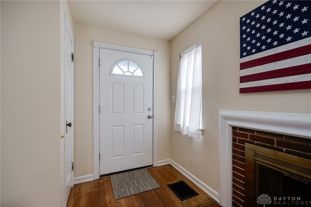 entryway featuring a brick fireplace, baseboards, visible vents, and wood finished floors