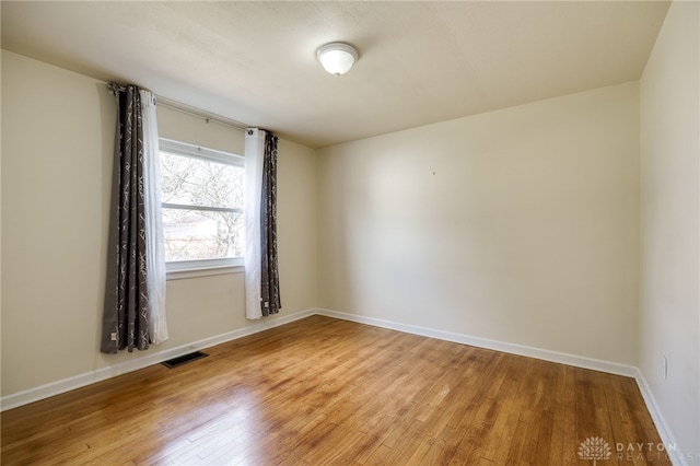 empty room with baseboards, visible vents, and light wood finished floors