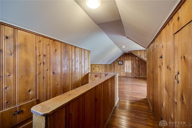 corridor with dark wood finished floors, vaulted ceiling, and wooden walls