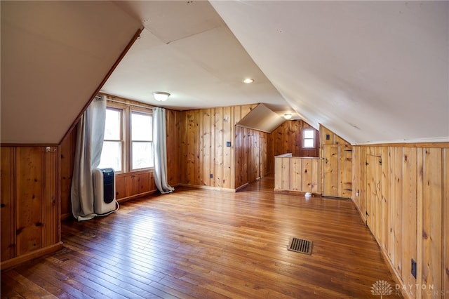 additional living space featuring lofted ceiling, visible vents, wooden walls, and hardwood / wood-style flooring