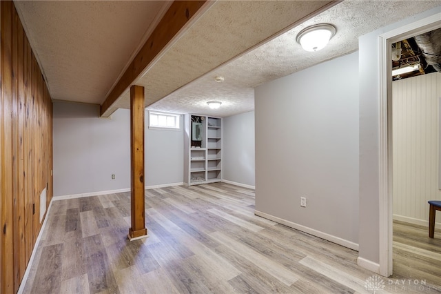 below grade area featuring wood walls, a textured ceiling, baseboards, and wood finished floors