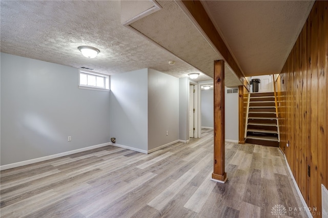 below grade area featuring a textured ceiling, wood finished floors, stairs, and baseboards