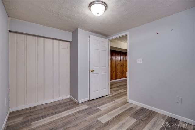 interior space with a closet, a textured ceiling, baseboards, and wood finished floors