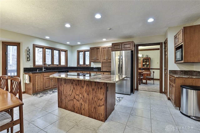 kitchen with light tile patterned flooring, a sink, a kitchen island, black appliances, and dark stone countertops