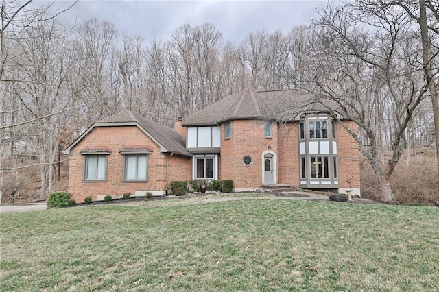 tudor house featuring a shingled roof, a front yard, brick siding, and a chimney