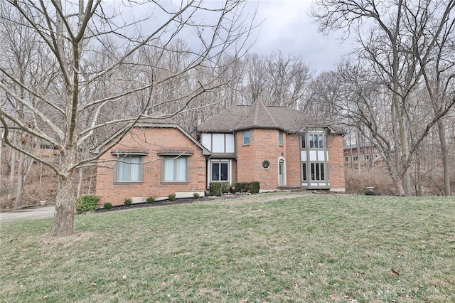 english style home featuring a shingled roof, a front lawn, and brick siding