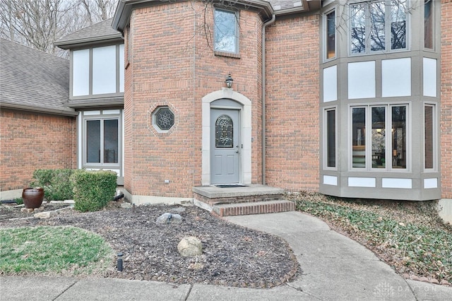 doorway to property featuring roof with shingles and brick siding