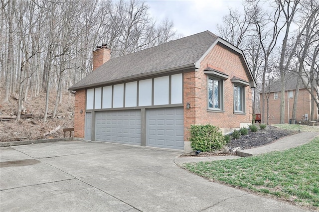 view of side of home with a garage, concrete driveway, a chimney, roof with shingles, and brick siding