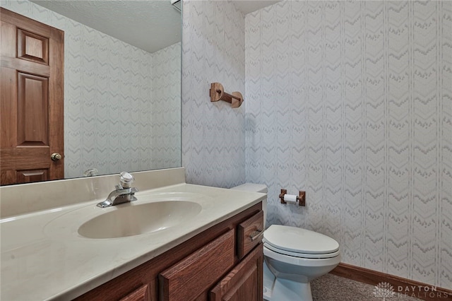 bathroom featuring toilet, vanity, and wallpapered walls