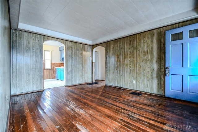 unfurnished room with arched walkways, wood-type flooring, and visible vents