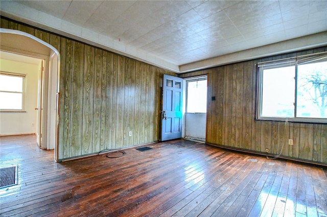 unfurnished room featuring arched walkways, wood walls, wood-type flooring, and visible vents