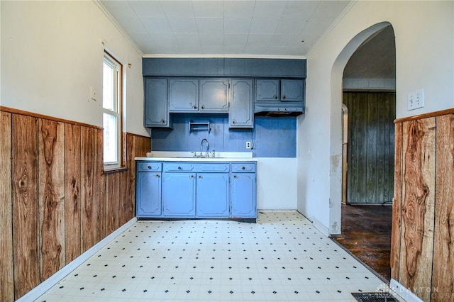 kitchen with arched walkways, a wainscoted wall, light floors, wood walls, and a sink