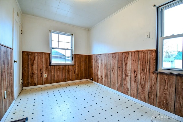 spare room with crown molding, wood walls, wainscoting, and tile patterned floors