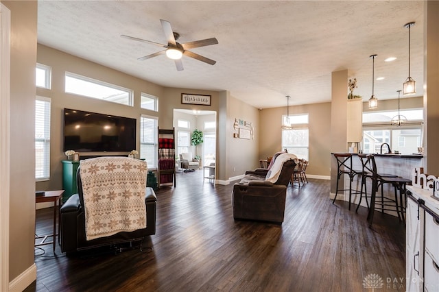 living area with a textured ceiling, ceiling fan, dark wood finished floors, and baseboards