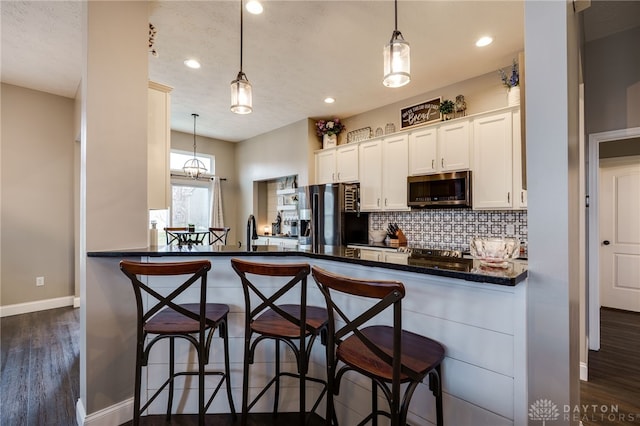 kitchen with a peninsula, white cabinets, appliances with stainless steel finishes, decorative backsplash, and dark wood finished floors