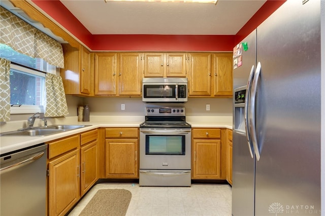 kitchen featuring appliances with stainless steel finishes, brown cabinetry, light countertops, and a sink