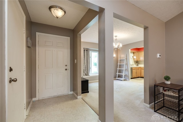 entrance foyer with light carpet, an inviting chandelier, baseboards, and a textured ceiling