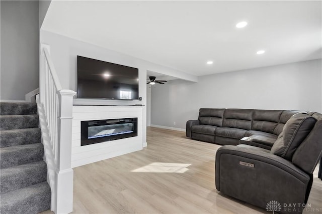 living room with recessed lighting, baseboards, stairway, light wood finished floors, and a glass covered fireplace