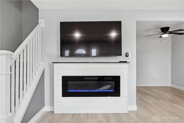 interior details featuring wood finished floors, a glass covered fireplace, a ceiling fan, and baseboards